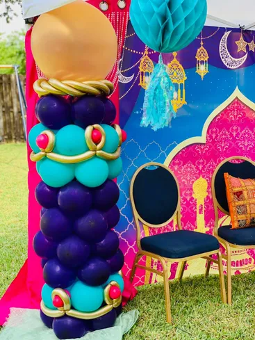 A tall purple, teal and gold balloon column beside a themed party backdrop.