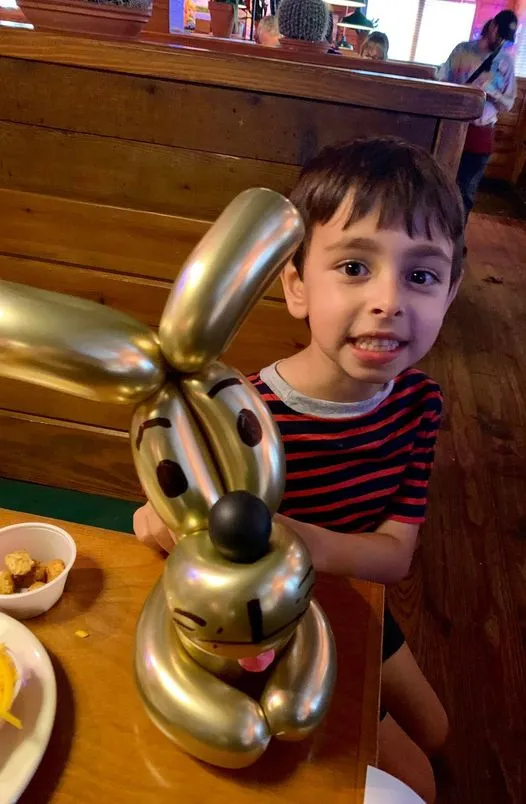 A boy holding a large gold balloon dog at a restaurant table.