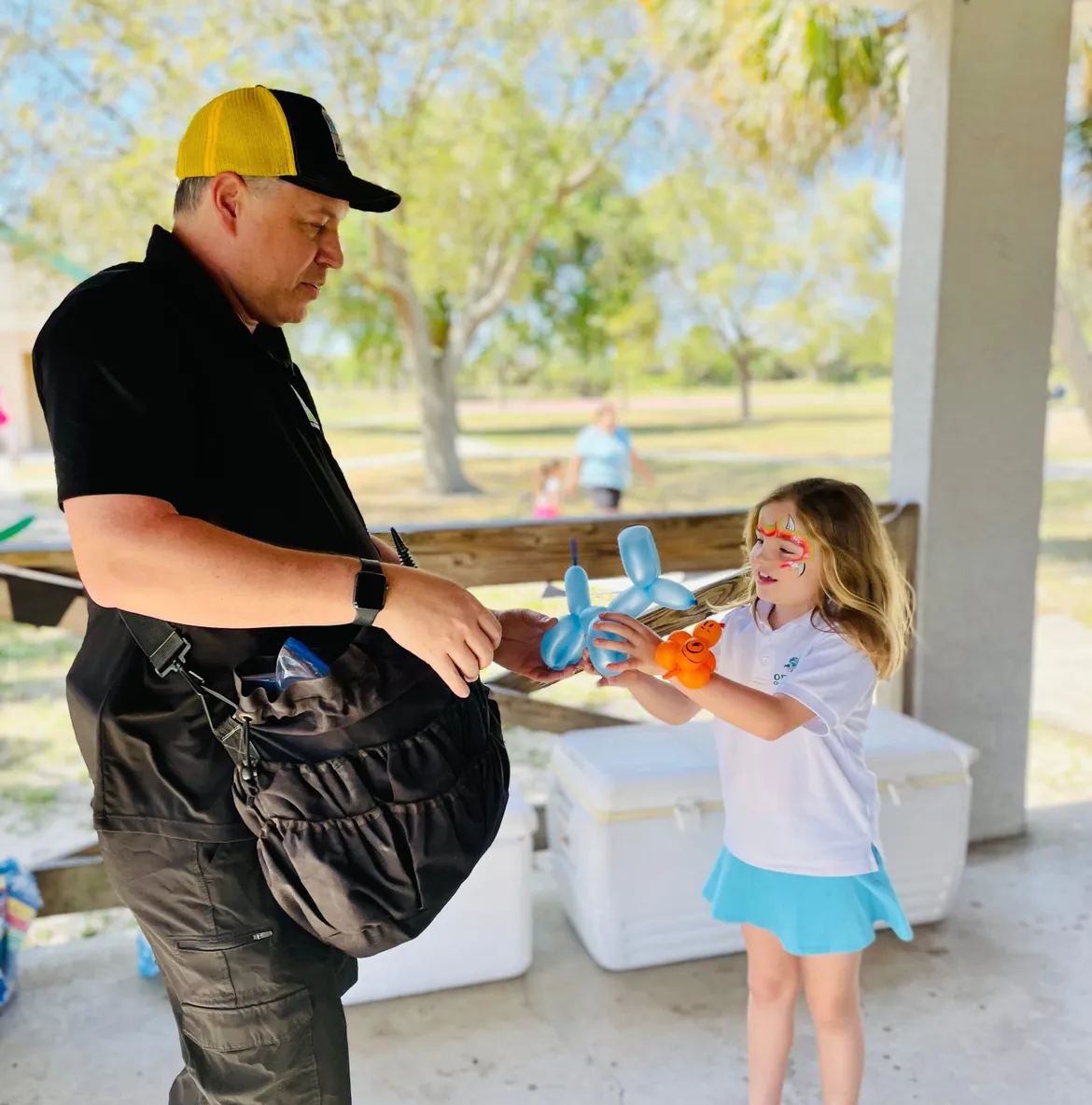 A Cheerioograms balloon artist handing a freshly twisted blue balloon dog to a young girl.