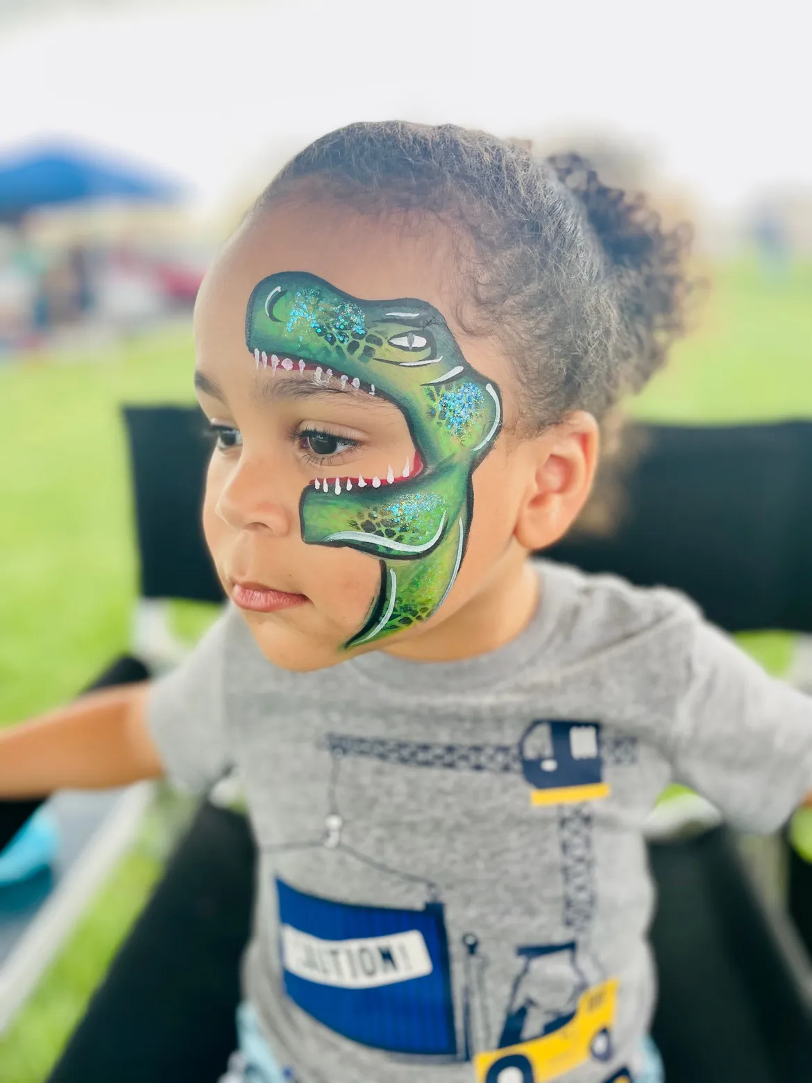 A child with a detailed green dinosaur design painted across one side of their face.