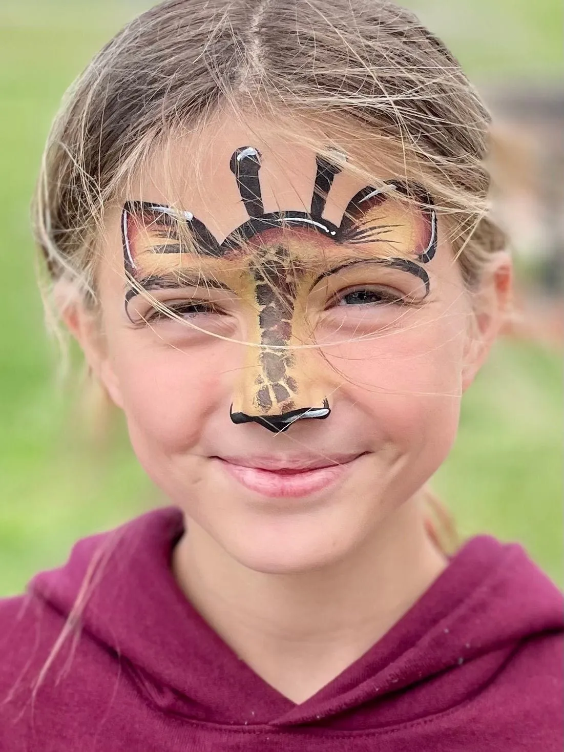 A child with a giraffe painted across their nose and forehead.