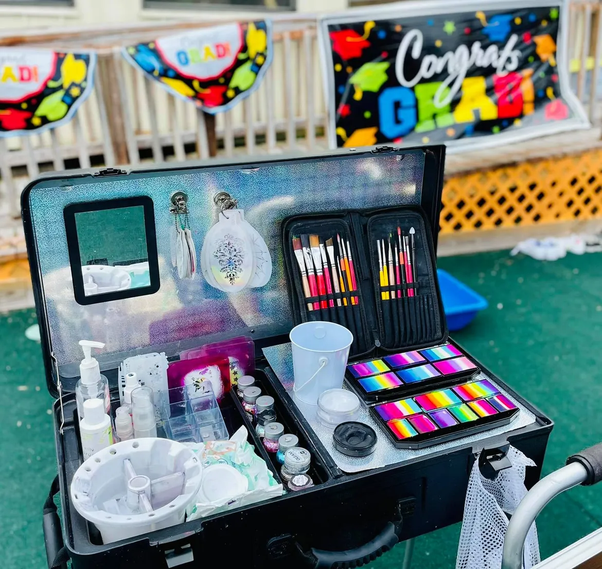 An open professional face painting kit showing brushes, split-cake palettes and glitter pots.
