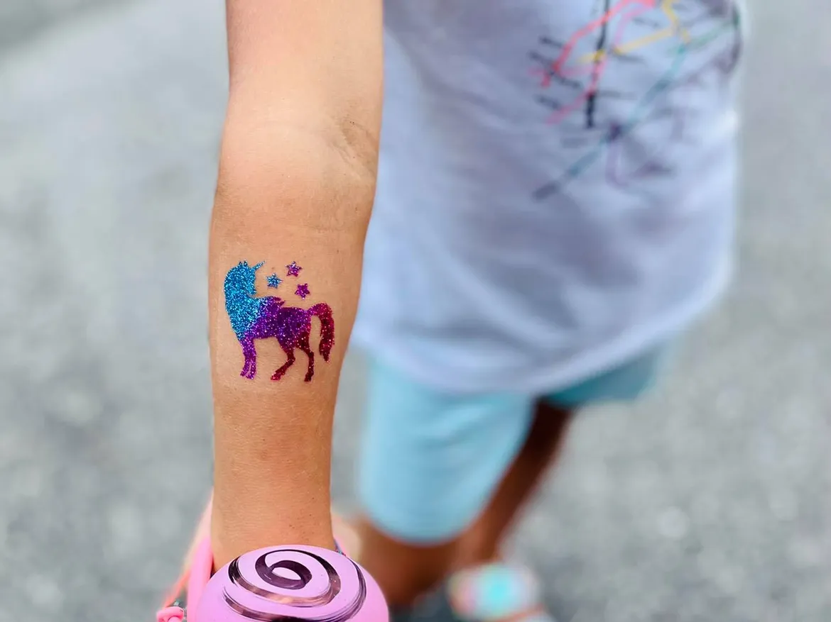 A sparkling blue and purple unicorn glitter tattoo on a child's forearm.