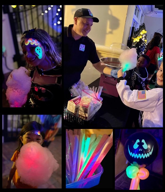 A glow party at night: a child with glow-in-the-dark ghost face paint holding lit cotton candy, a Cheerioograms host spinning cotton candy, glow sticks and a glowing jack-o'-lantern balloon.